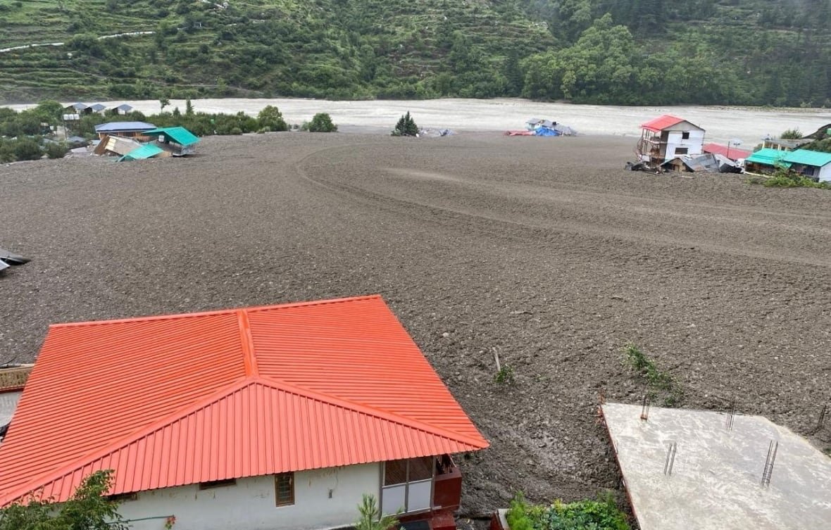 A house with a terracotta roof is shown in the foreground, and then a massive flood of mud fills a large space, with some tipped-over houses visible at the edges in the distance. 