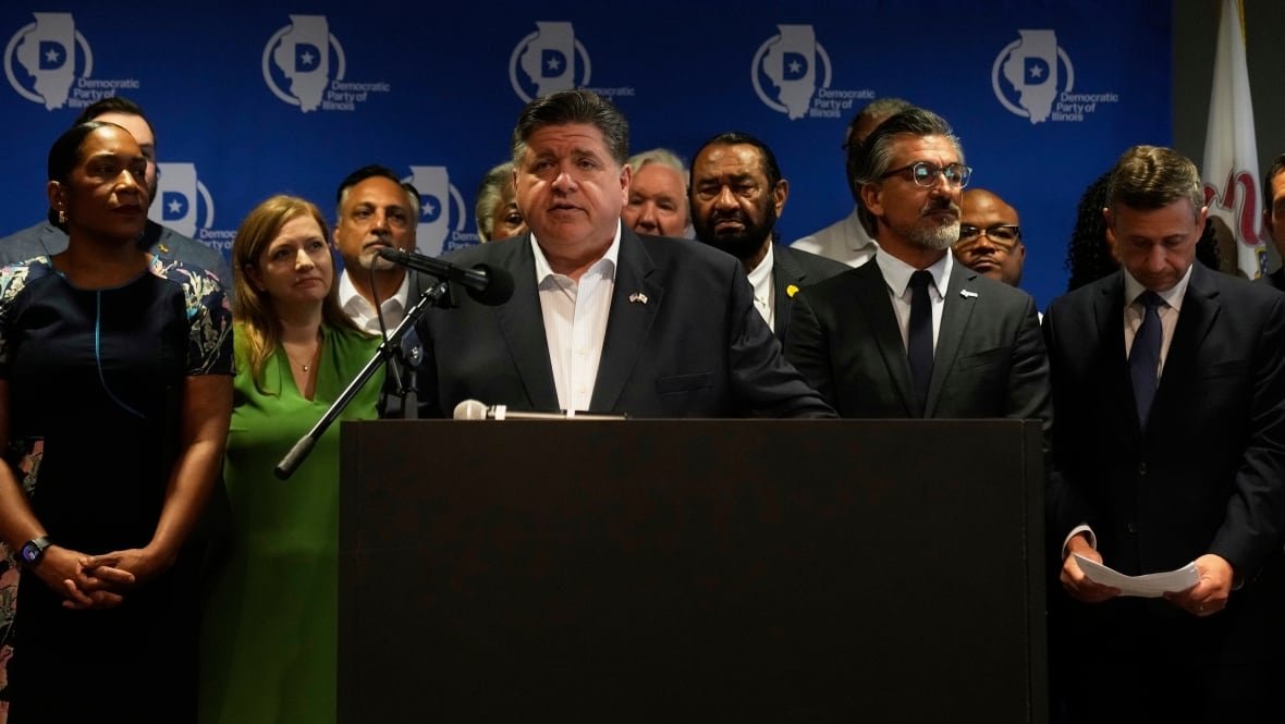 Illinois Gov. JB Pritzker stands at a podium, with several Democrat state legislators from Texas behind him. 