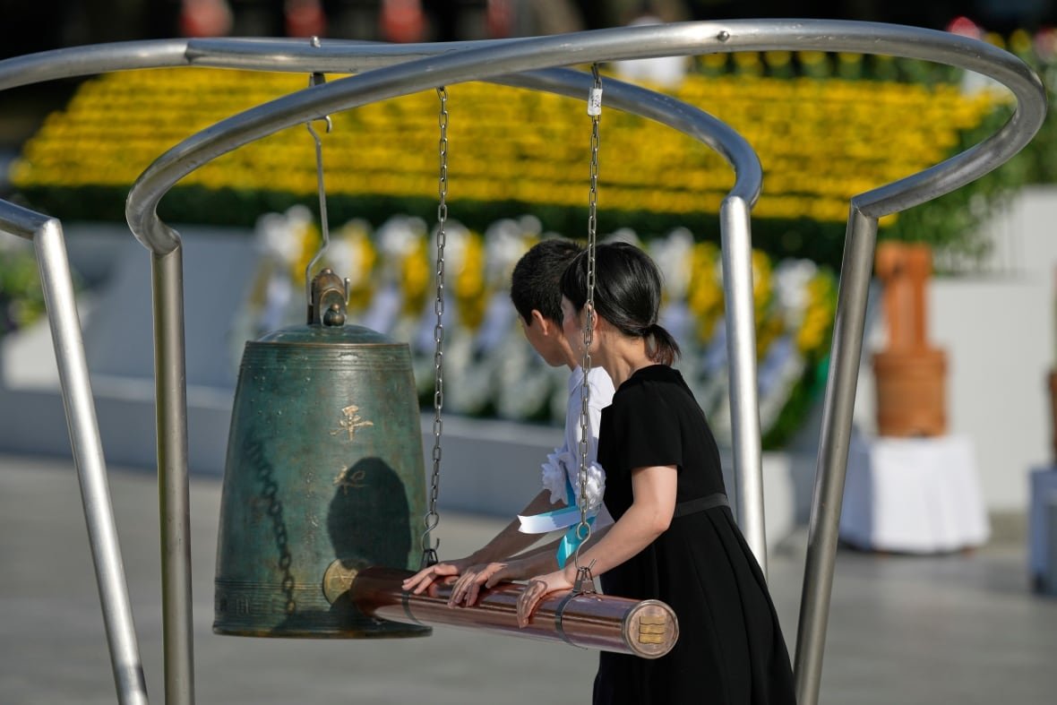 Two people with dark hair are shown from behind using a large item to ring a bell.