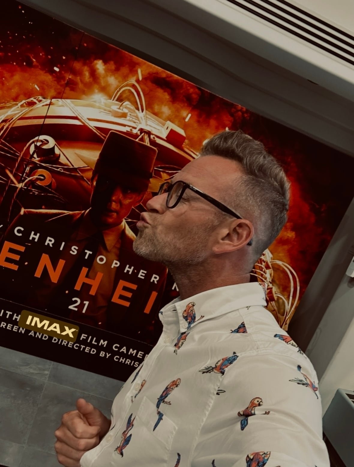 Man standing in front of an Oppenheimer movie poster. 