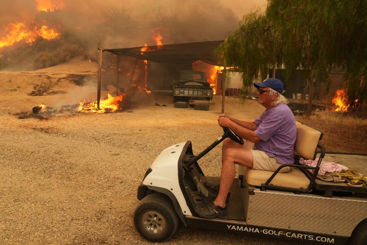 A resident rides a golf cart while exiting his property amid a wildfire burning in Halsey Canyon, Calif.