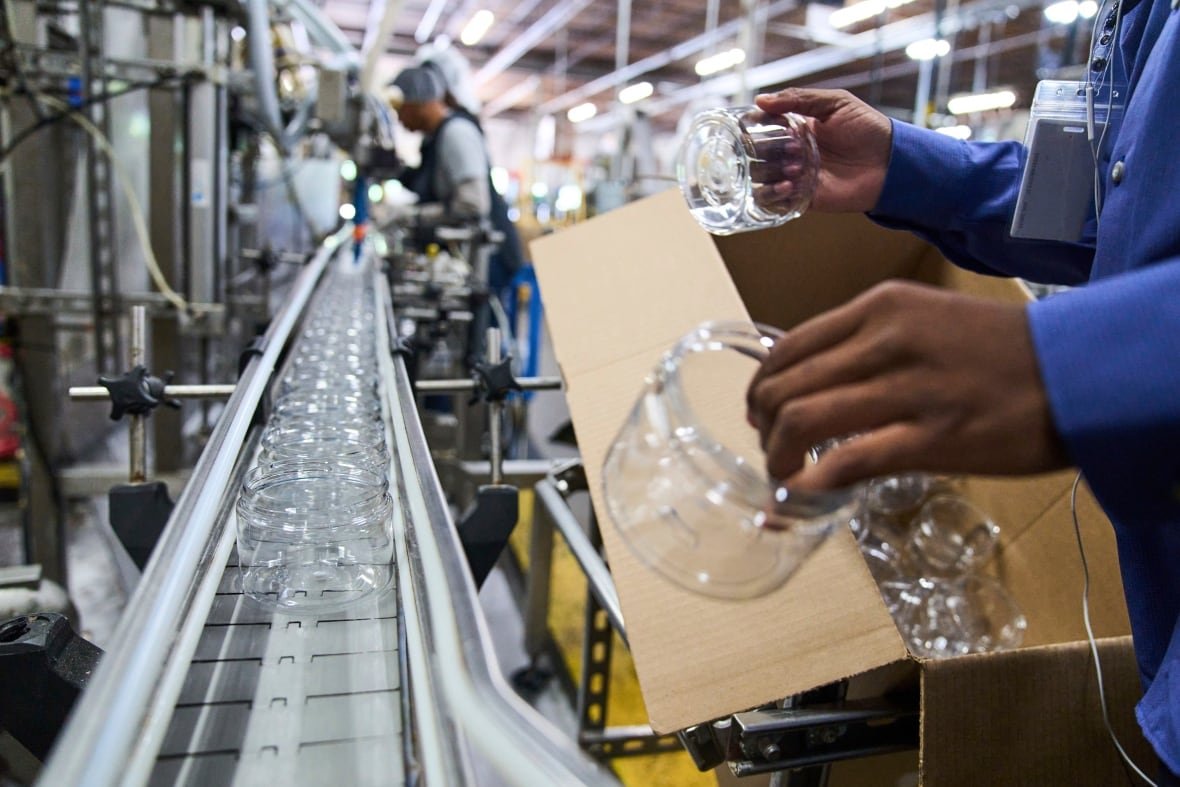 A factory worker places clear plastic jars on a conveyor belt.