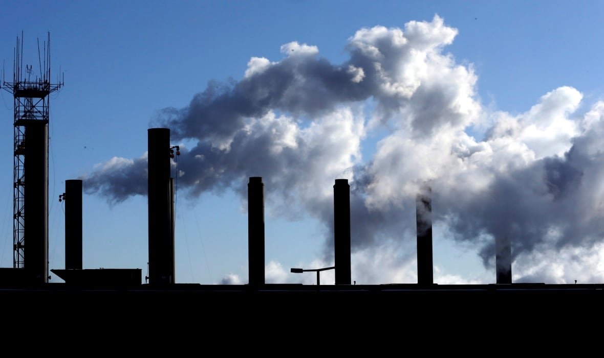 Factory chimneys and their emissions are silhouetted against a blue sky.