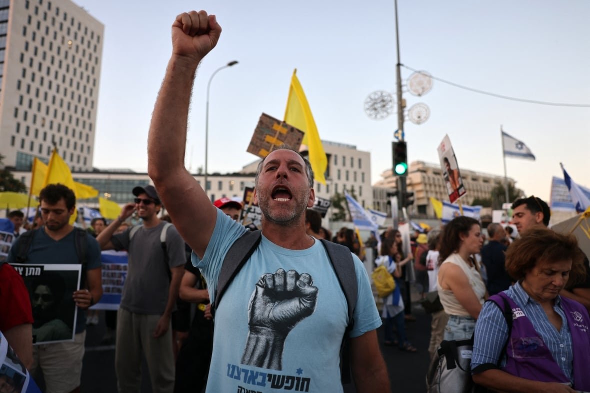 A man wearing a light blue T-shirt raises his fist in the air as he shouts, during a demonstration outside.