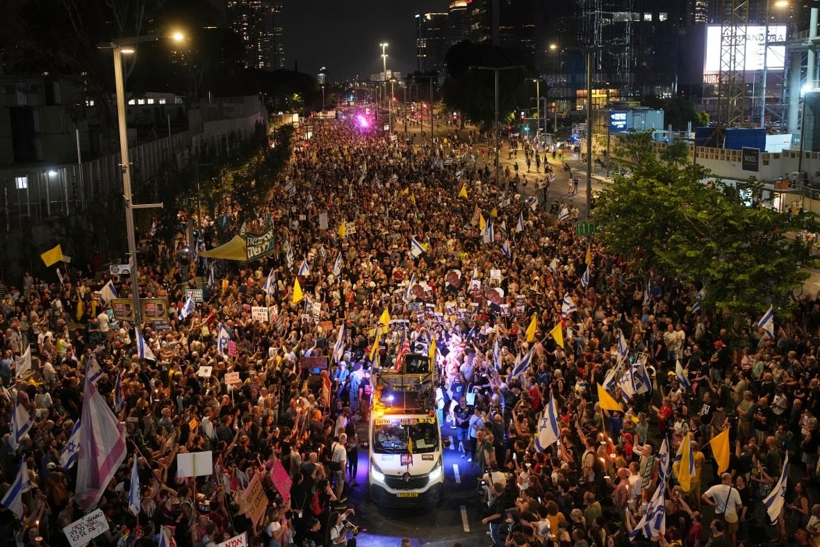 A protest at night fills a street several hundred metres back.