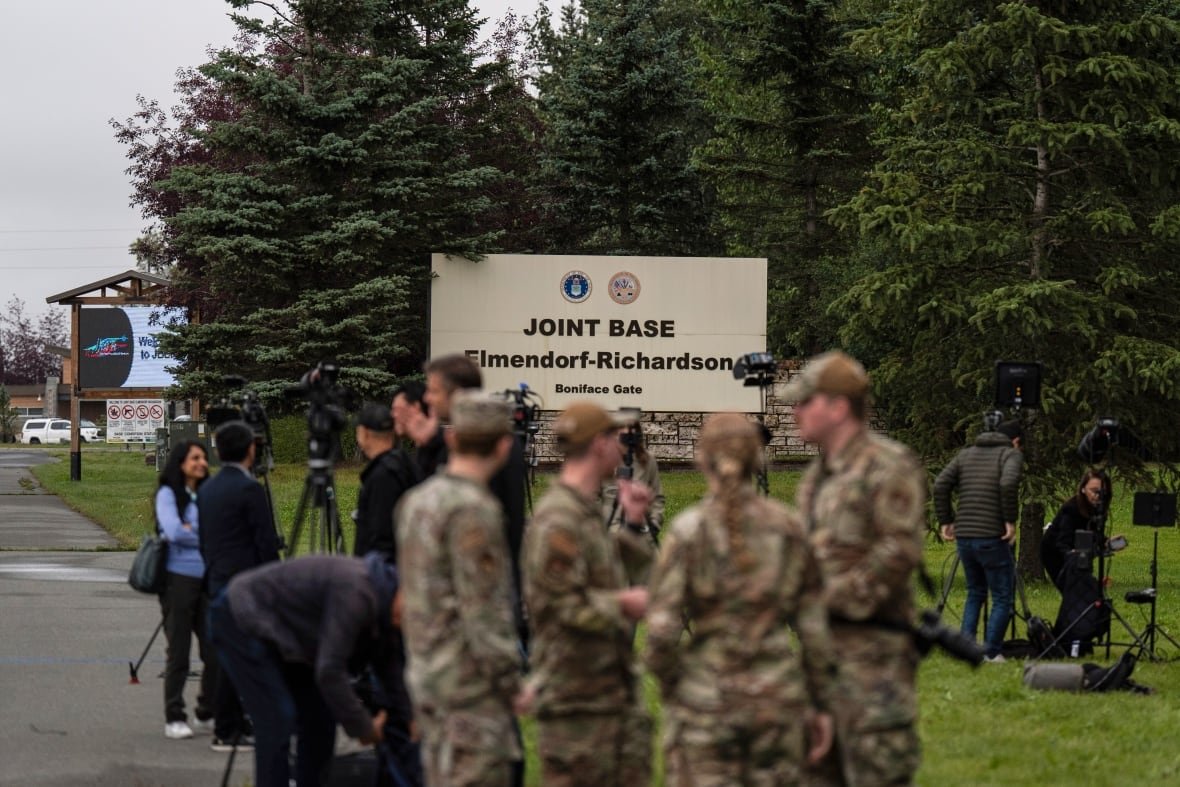 Military personnel and the media stand outside Joint Base Elmendorf-Richardson in Anchorage, Alaska, Thursday, Aug. 14, 2025, ahead of a meeting between President Donald Trump and Russia's President Vladimir Putin.