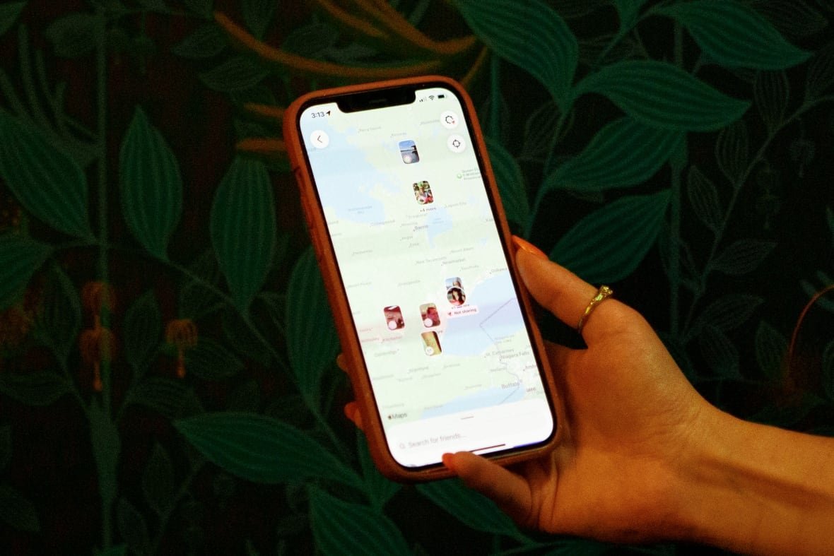 A hand holds an iphone, and on the screen a map is visible that shows users' pinned locations.