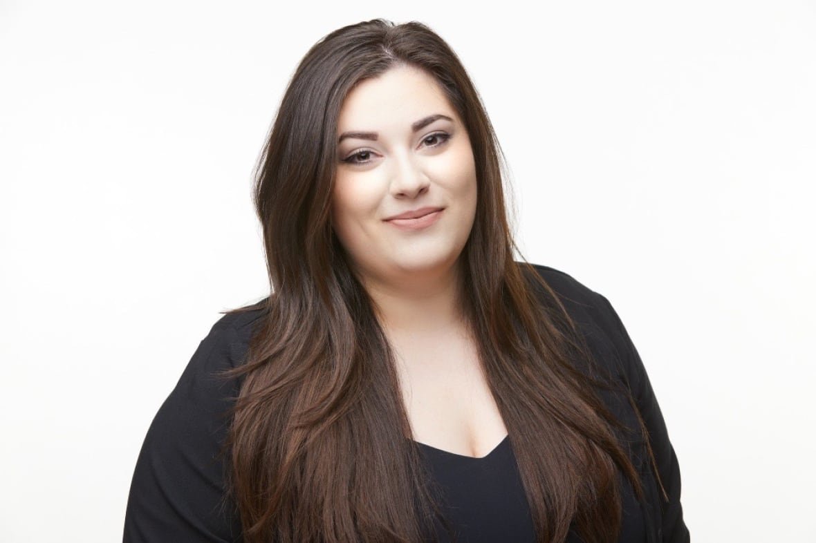 A woman with dark hair and a dark long sleeve shirt smiles at the camera for a headshot photo.