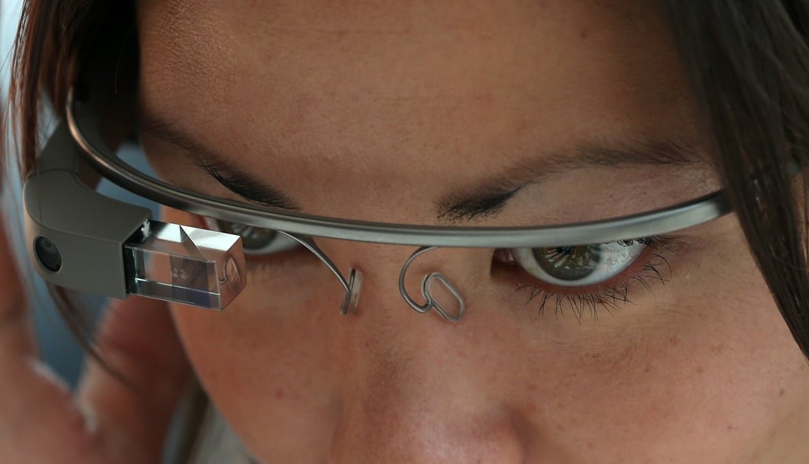 A woman is shown in close-up wearing a pair of smart glasses.