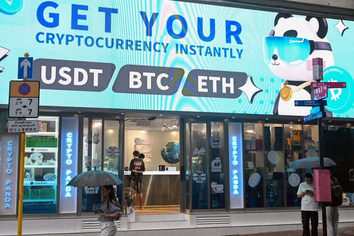 People walk outside a storefront advertising cryptocurrencies.