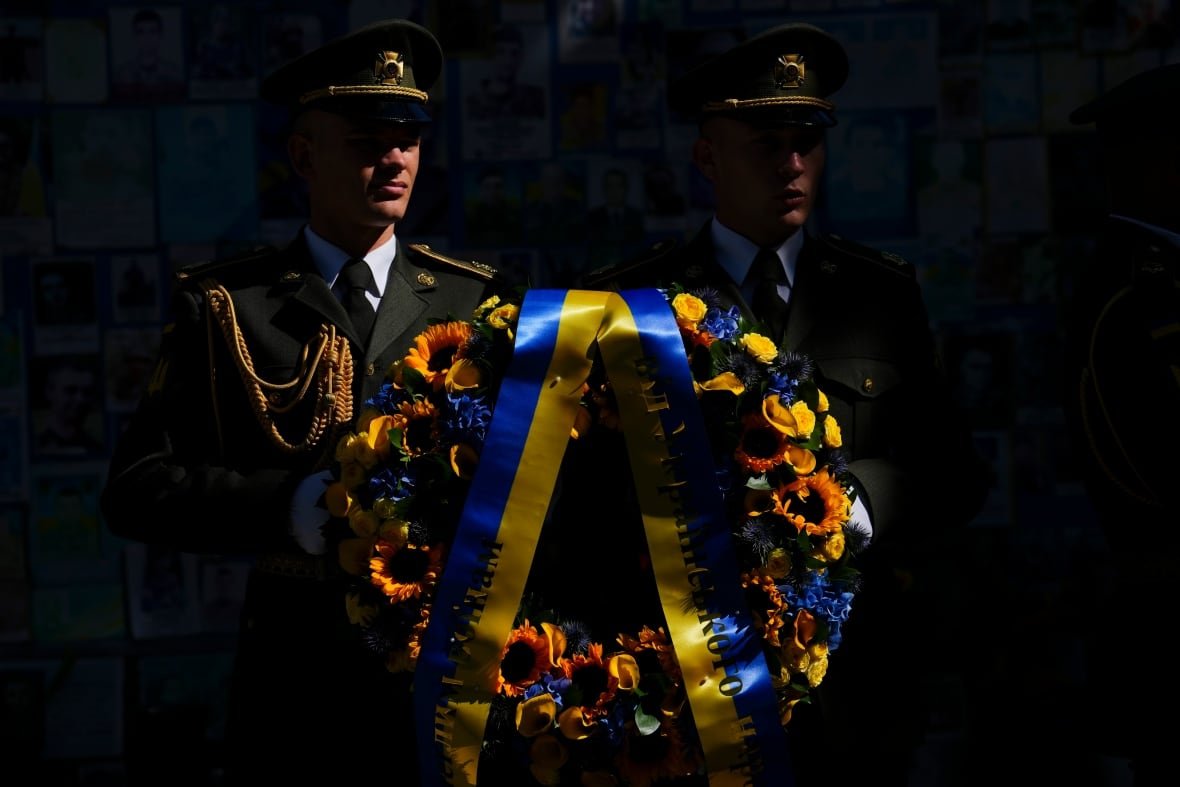Two soldiers stand in the sunlight against a dark background.