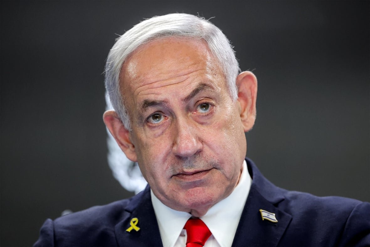 A closeup shot of a man with white hair wearing a navy blue suit.