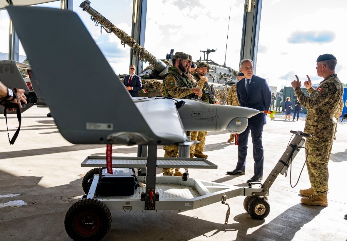 A drone can be seen in the foreground as military members walk around it, alongside Prime Minister Mark Carney.