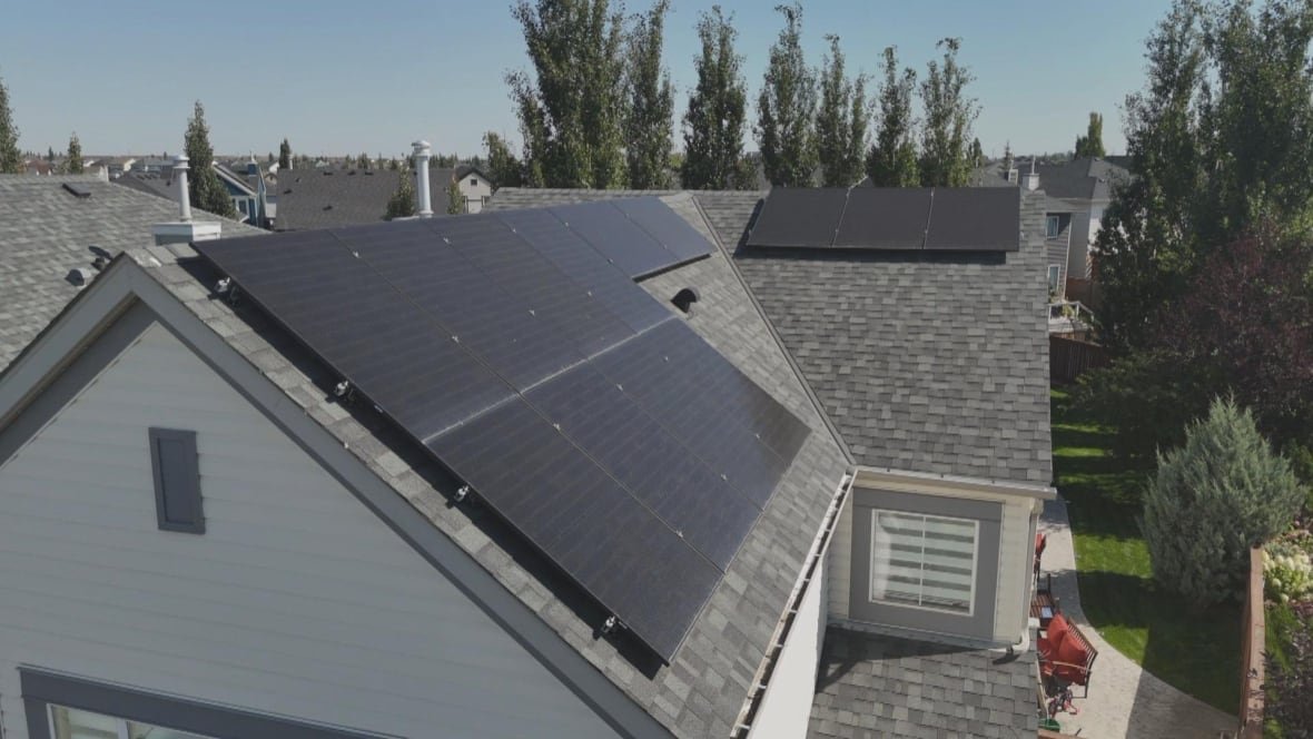 An image taken with a drone camera shows several solar panels on the roof of a home. 