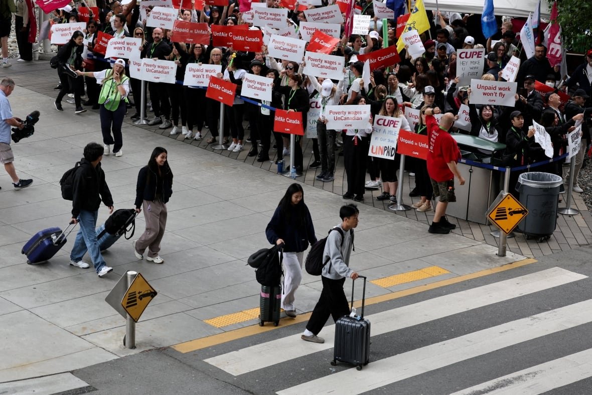 Passengers walk in front of demonstrators holding placards at the Vancouver International Airport Aug. 17, 2025 as Air Canada flight attendants said they will remain on strike.