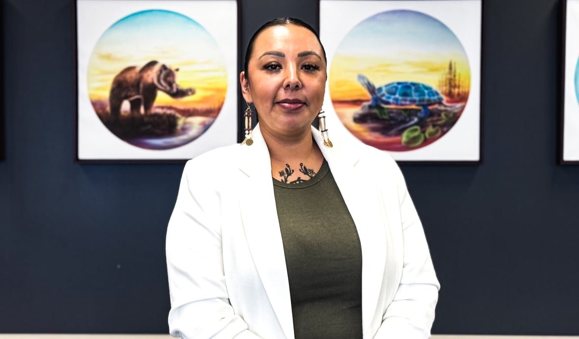 A woman wearing a white blazer and green t-shirt stands in front of four framed images of animals with her hands clasped in front of her.