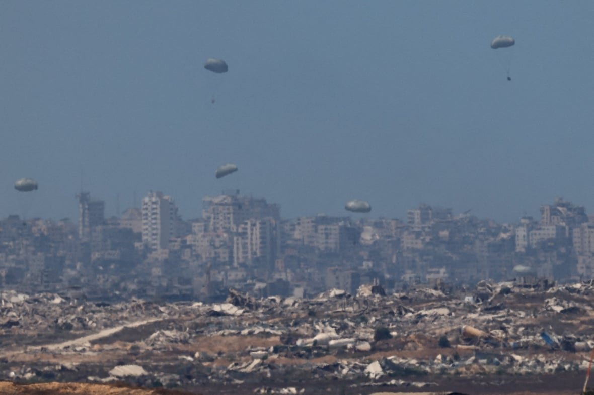Parachutes carrying aid fall over a destroyed city.
