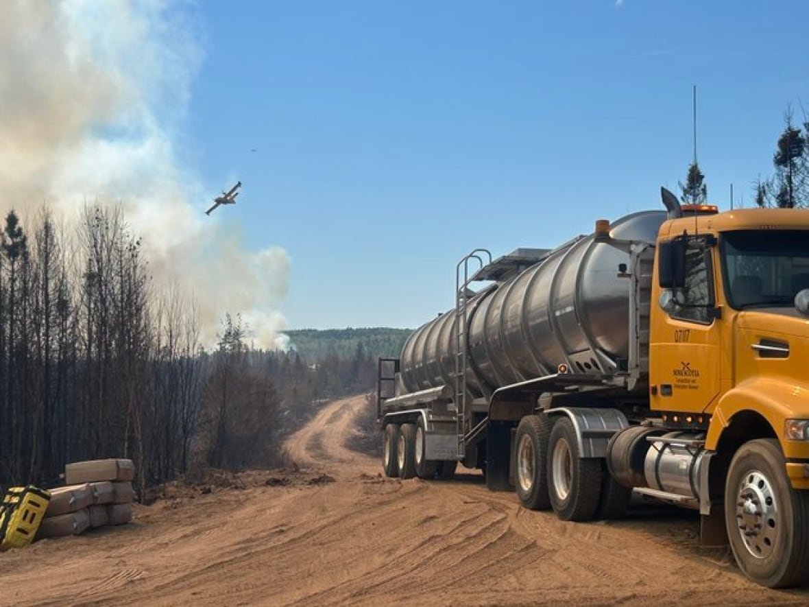 A tanker truck is shown with a long dirt road behind it and smoke and an airplane in the background.