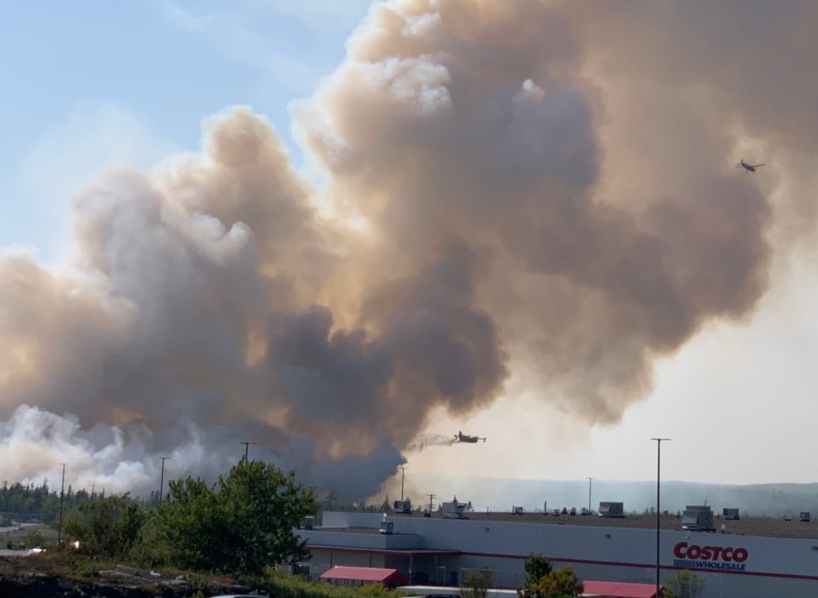 Smoke billows into the air as two planes fly by. A commercial building is in the foreground.