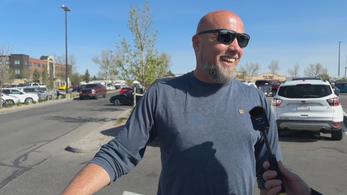 A man stands in the sunshine in a parking lot.