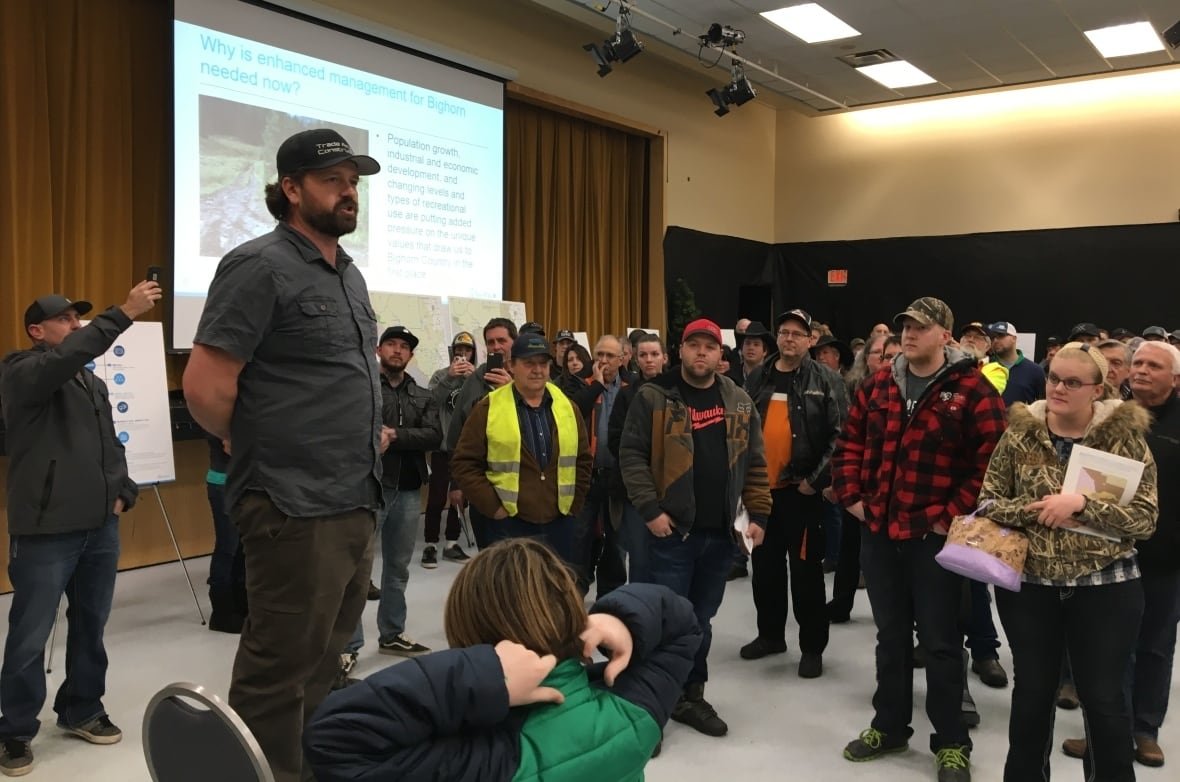 A man stands on a chair to address a crowd with a screen behind him that says Bighorn.