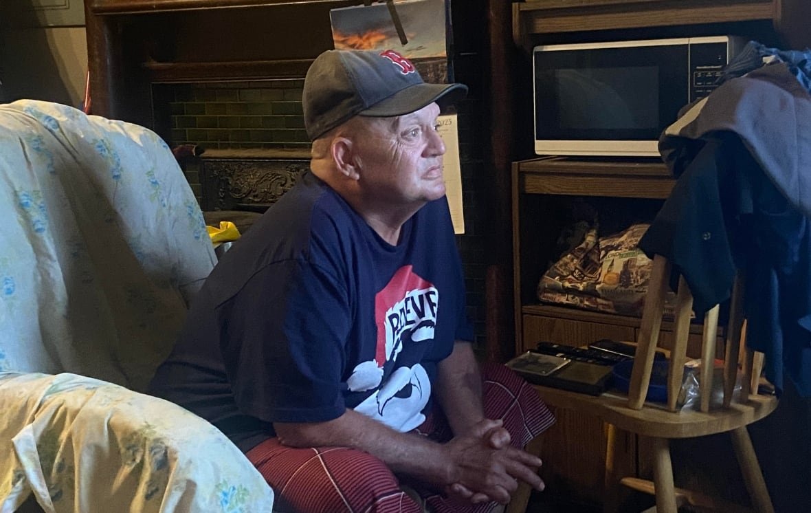 older man facing to the right, wearing baseball cap and sitting in an armchair