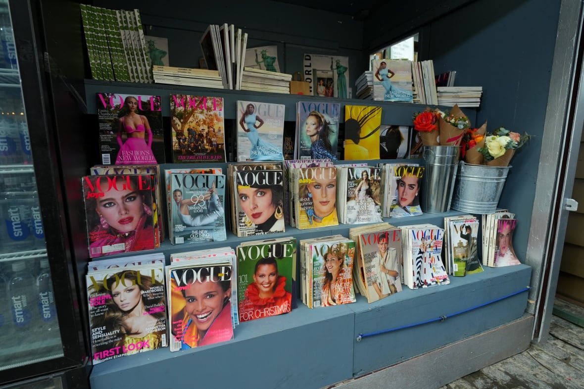 A newsstand with various issues of Vogue magazines on the shelves.