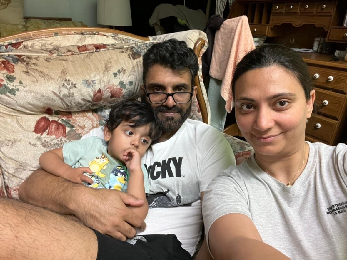 A woman, man and toddler are seen in a selfie, sitting on a couch.
