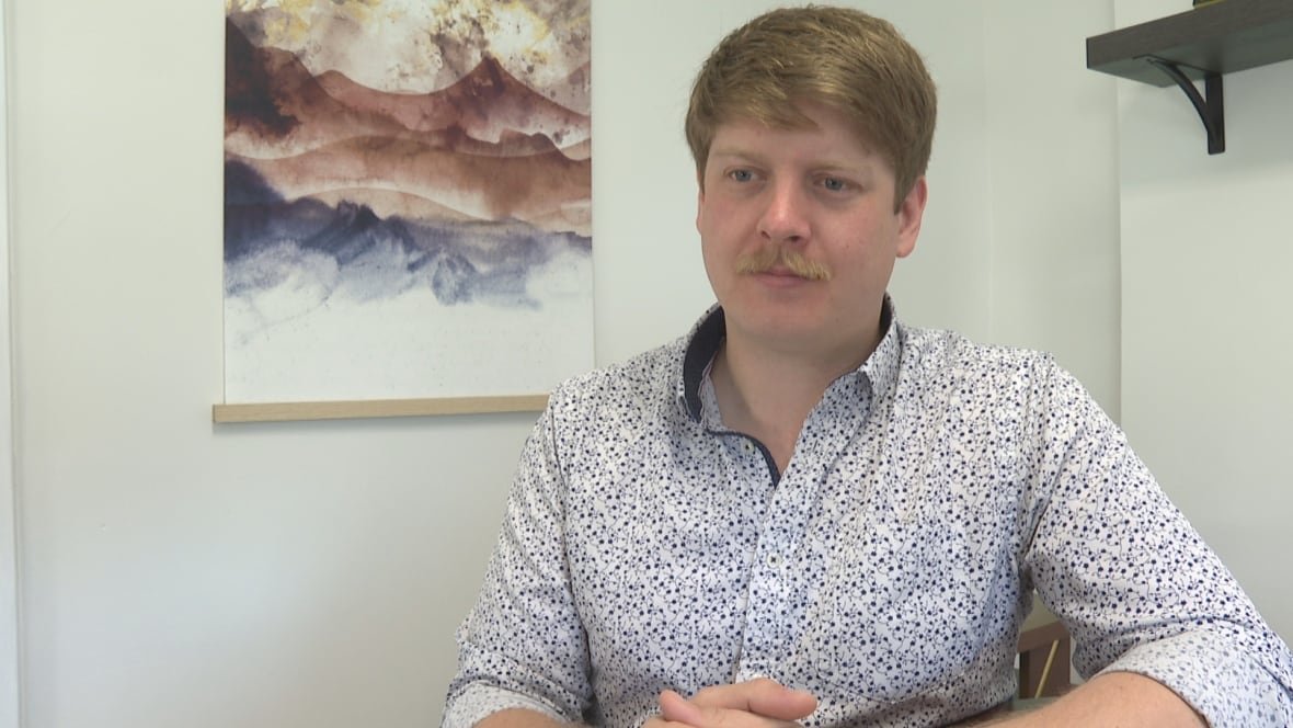 A man in a blue and white print shirt sits in an office. 