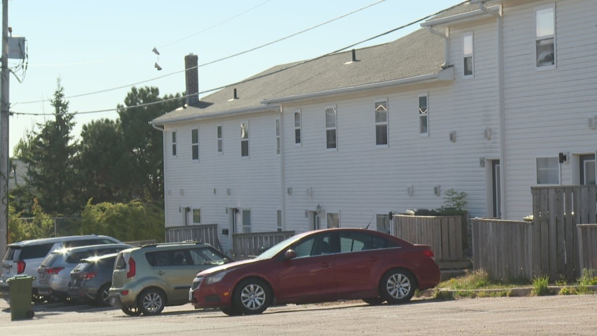 A number of white-sided townhouse units in an apartment complex, with cars and SUVs parked outside.