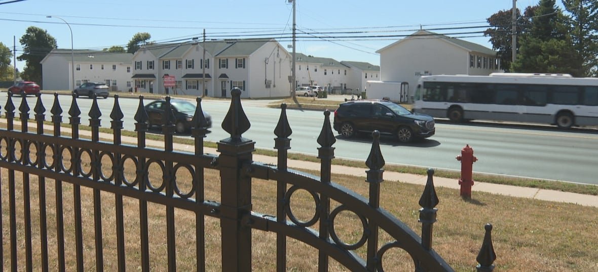 Cars and a bus travel along a city street with several apartment buildings in the background. 