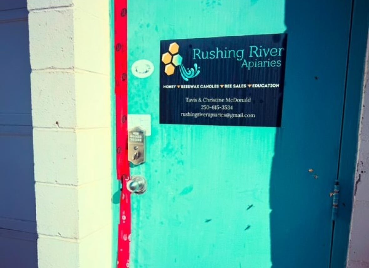 A blue door with a Rushing River Apiaries sign taped up with red tape.