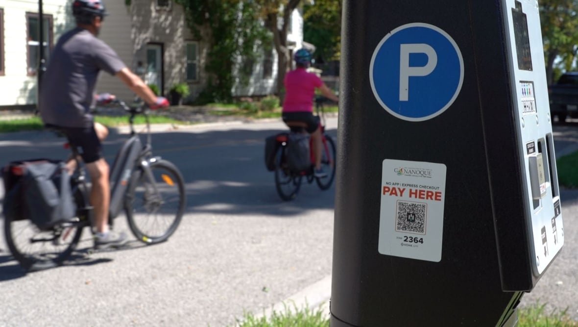 Cyclists pass a roadside parking metre on a sunny day.
