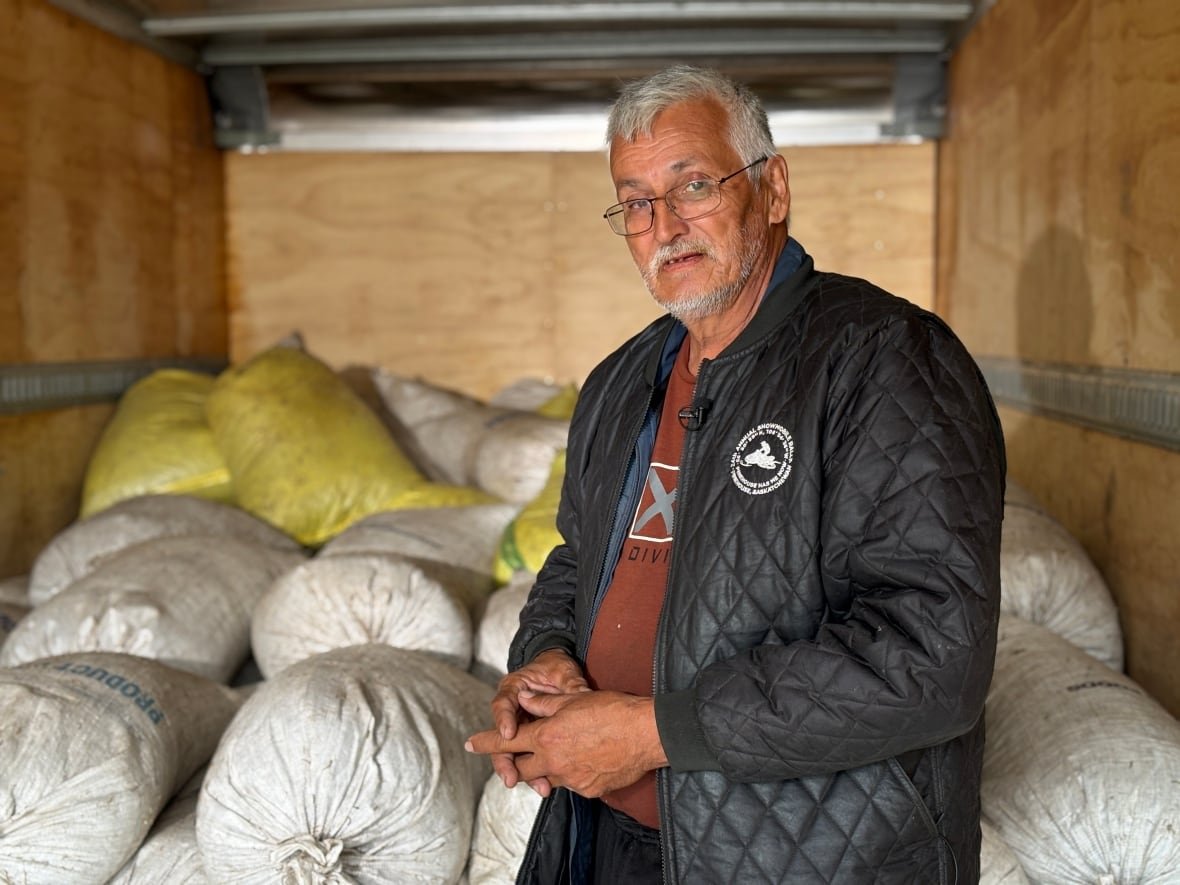 Man in black jacket stands inside truck with large white bags behind him