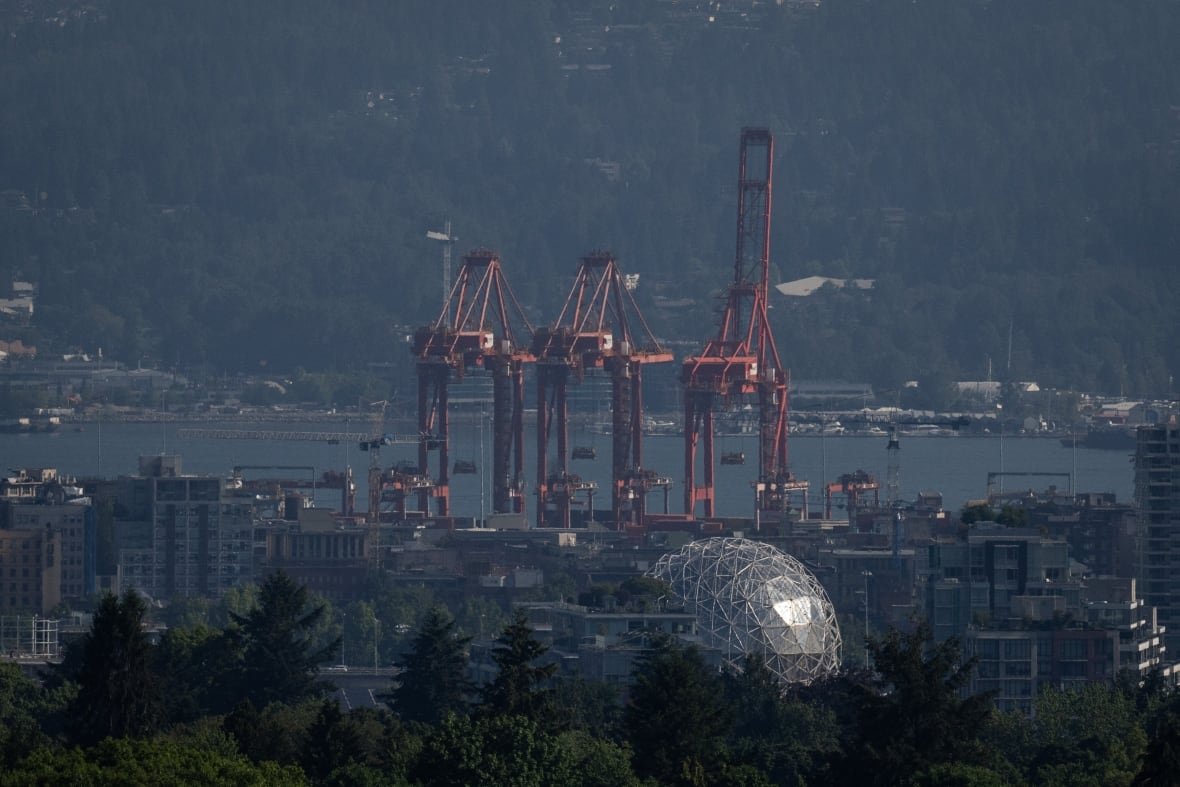 Port loaders are seen next to a spherical building on a hazy day.