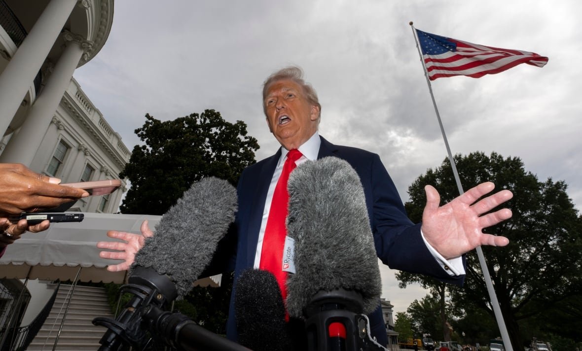 U.S. President Donald Trump, with microphones in the foreground and the U.S. flag and the White House in the background. 