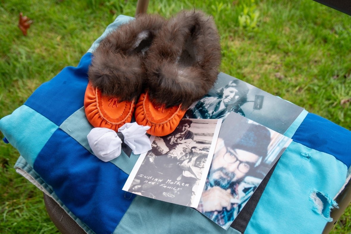 A pair of orange moccasins are seen on a blue blanket, along with a white pouch of tobacco and three printed photographs.