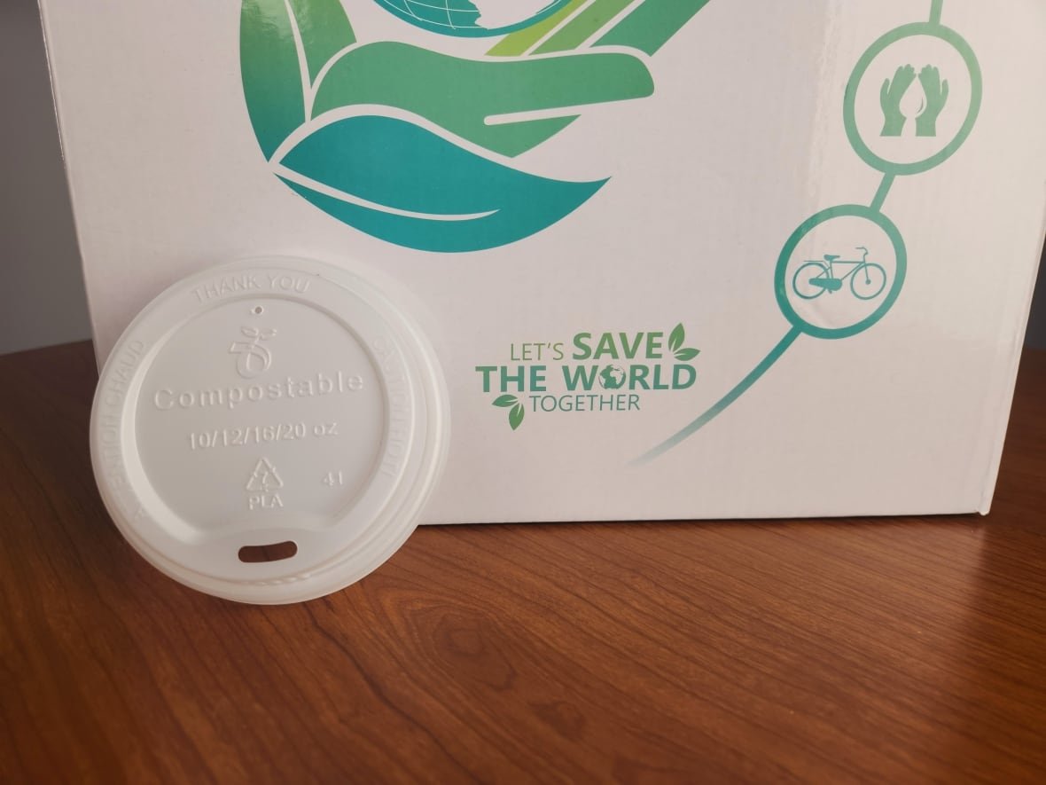 A plastic coffee lid leans against some compostable packaging.