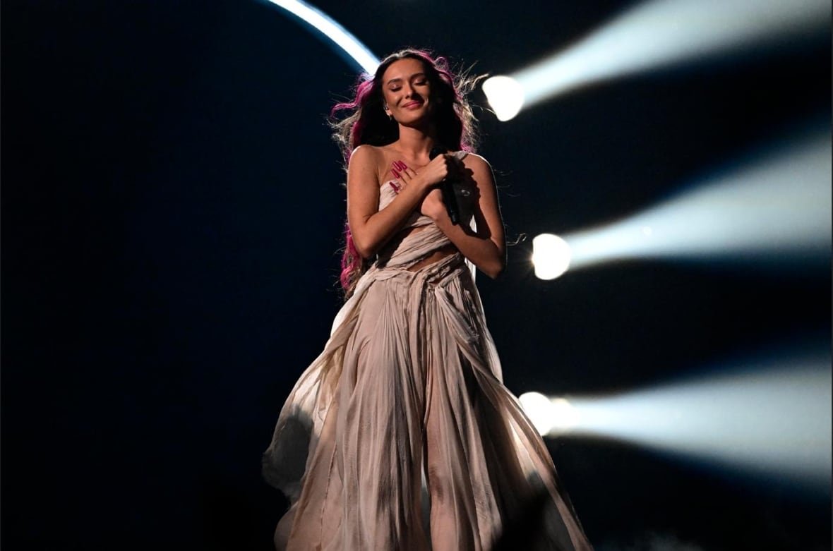 A singer smiles while folding their arms over their chest during a performance.