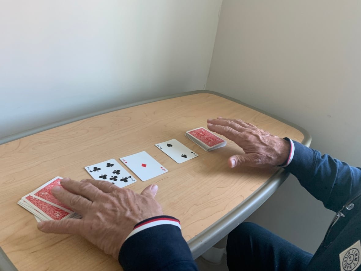 A man's hands playing solitaire with a deck of cards on a wooden table.