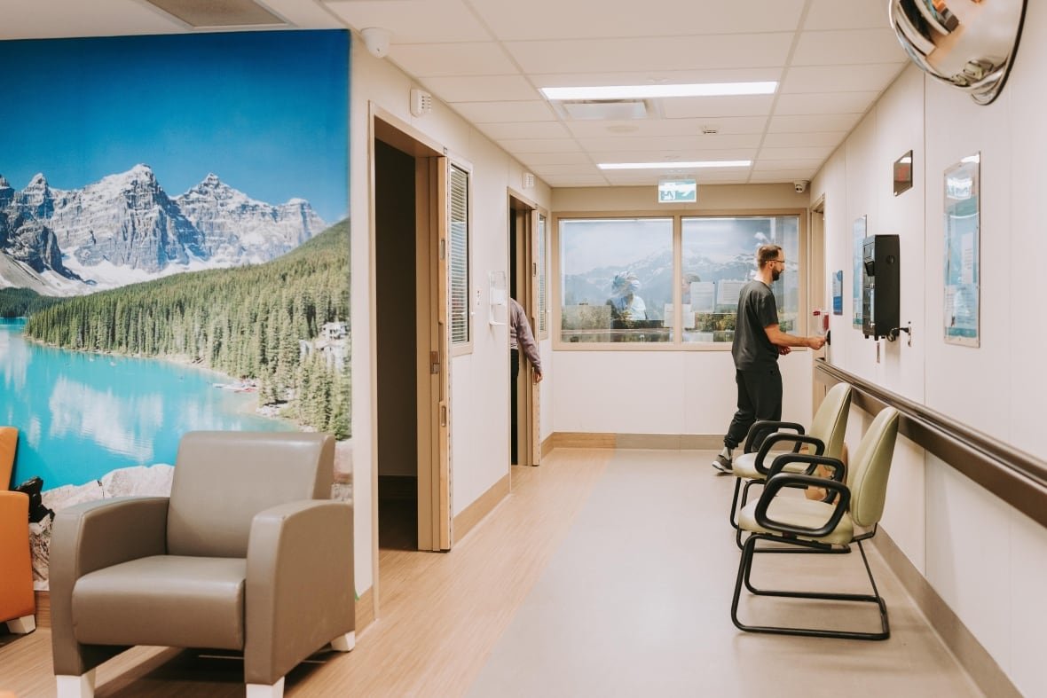 A doctor in scrubs works in a waiting area that has a nature mural of a mountain, trees and a lake
