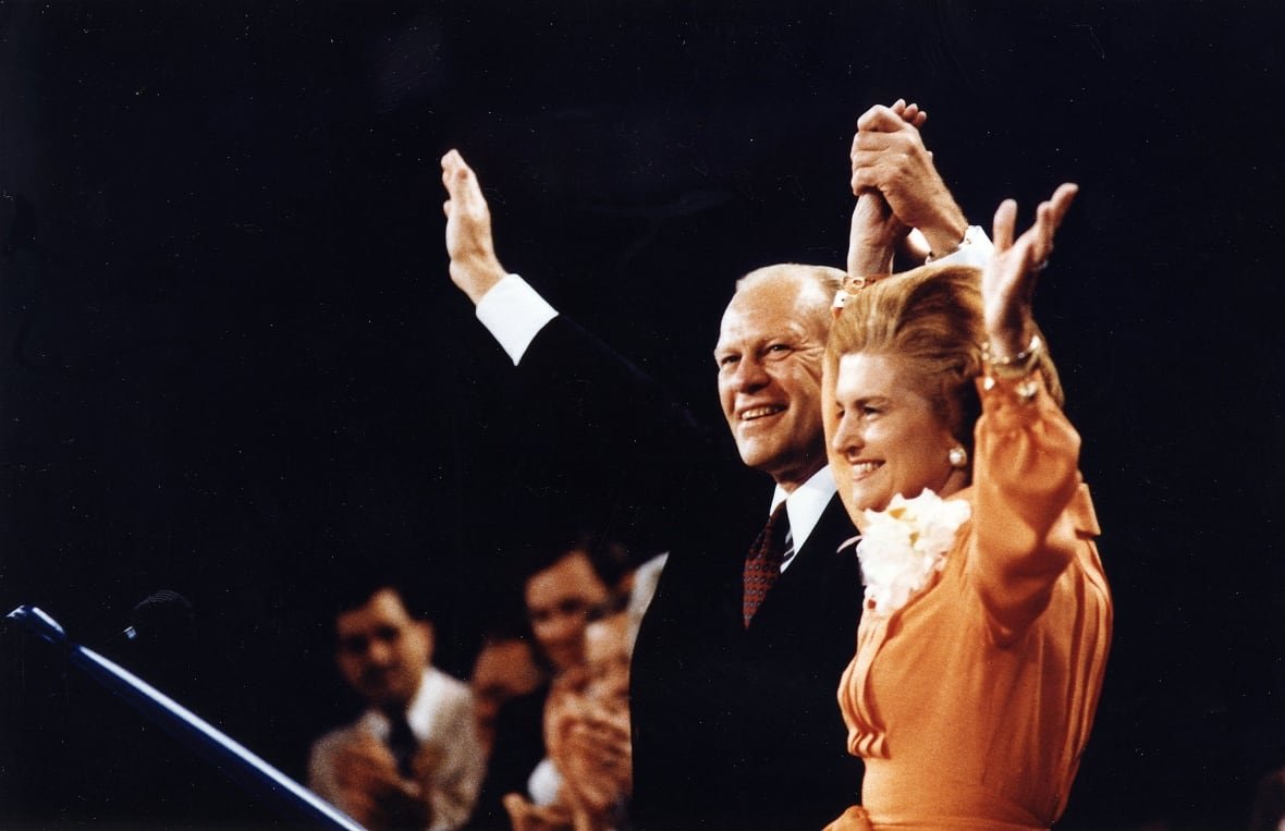 A balding cleanshaven man and a woman in a frilly blouse are shown in profile raising their arms in a colour photo that appears to be decades old.