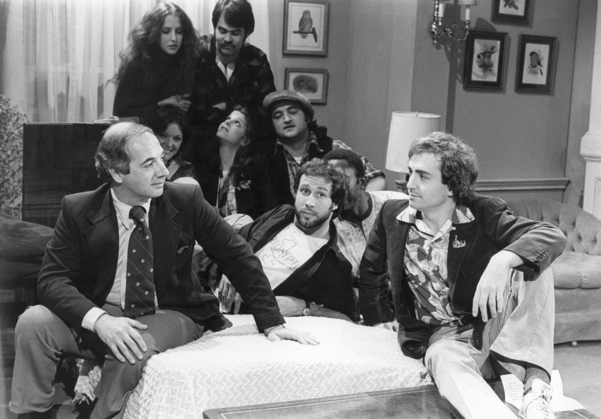Several people, mean and women, are shown seated on a stage setup in a black and white photograph that appears several decades old.
