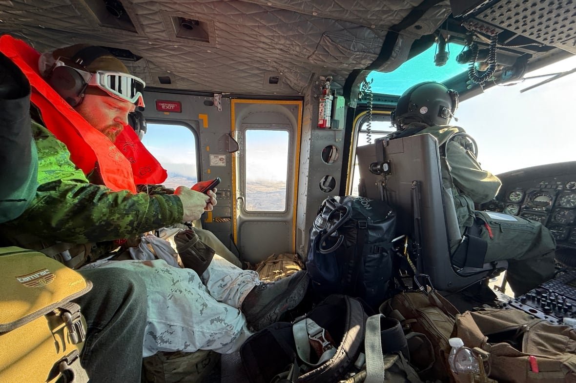 A soldier and pilot sit in the cramped interior of military helicopter. 
