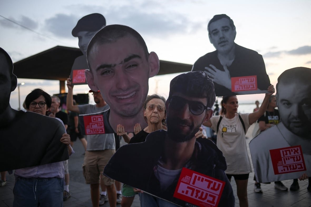 A crowd of protesters carry large images of men and women. 