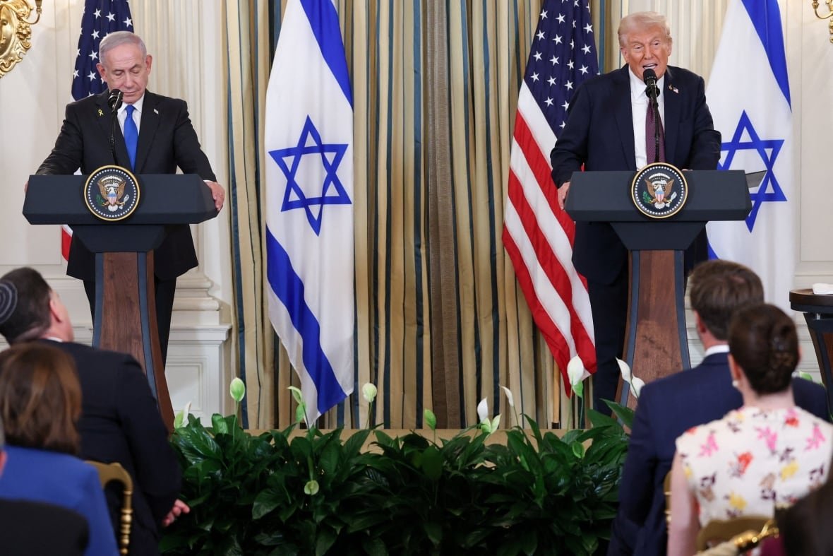 Two men stand at lecterns. There are American and Israeli flags in the background.