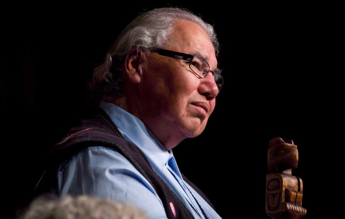 A man in a shirt and vest has an attentive look as he listens to an unseen person.