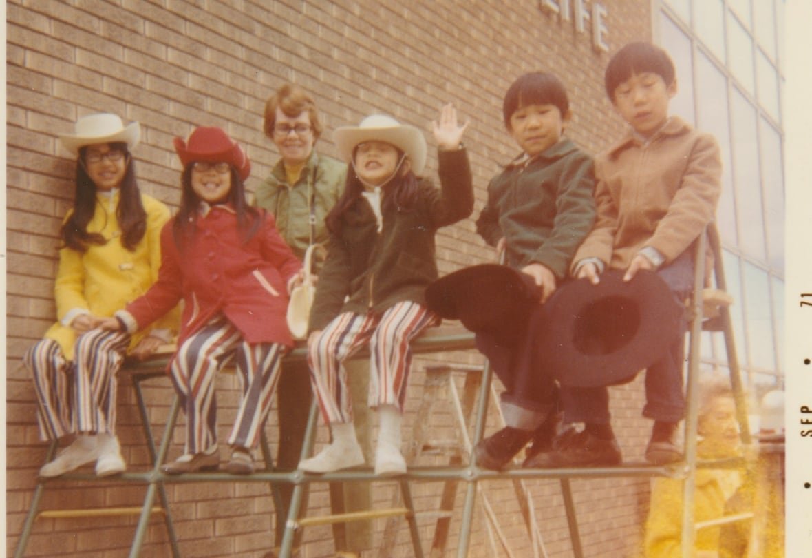 Five children sit on top of a set of metal bars and smile at the camera.