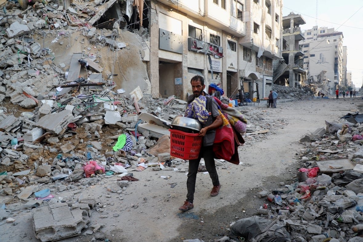 A man carries belongings as he walks through a damaged street.
