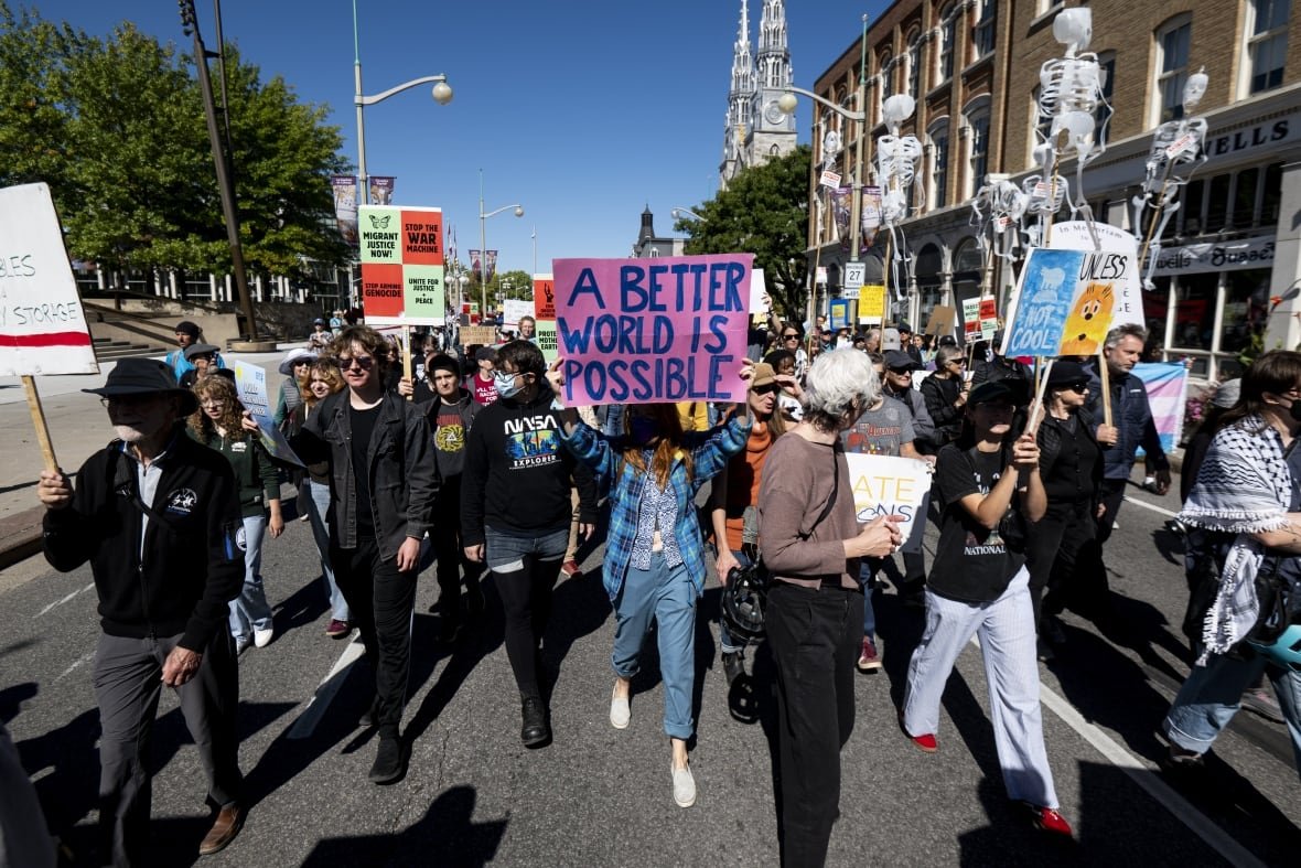 A group of people carrying protest signs walks down a city street on a sunny day.